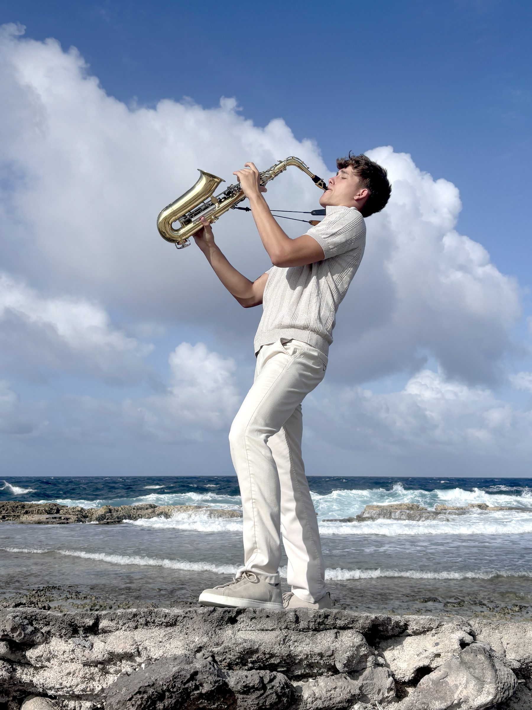 Kian Kazàn playing saxophone on a rocky shore against a dramatic sky